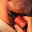 Close-up of stubbled lower face with Beardbrand Fox Hunt Eau de Parfum roll-on bottle held against the skin.